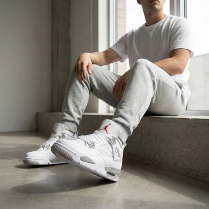 Person wearing white sneakers with a red logo, sitting on a windowsill.
