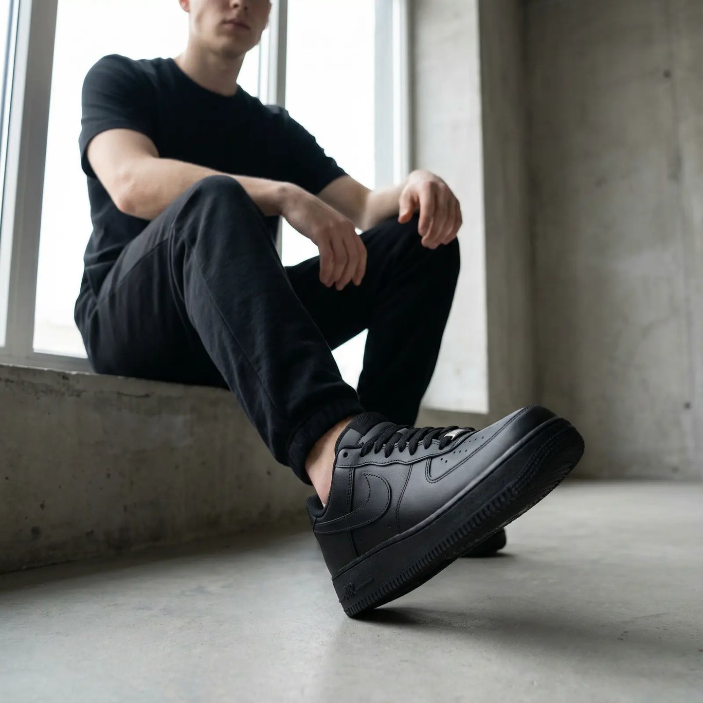 Person wearing black sneakers sitting by a window in a minimalistic setting