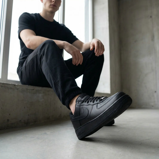 Person wearing black sneakers sitting by a window in a minimalistic setting