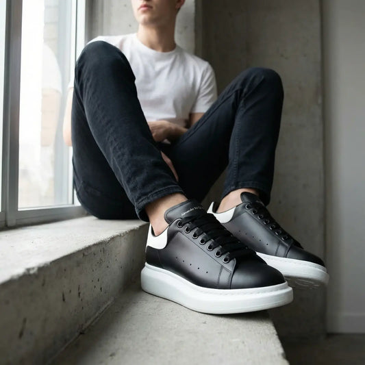 Person wearing black sneakers with white soles sitting by a window.