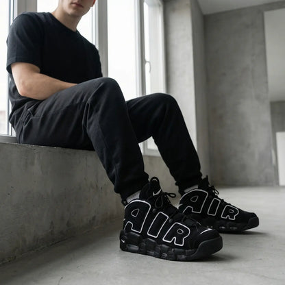 Person wearing black sneakers with 'AIR' branding, sitting in a minimalistic room.