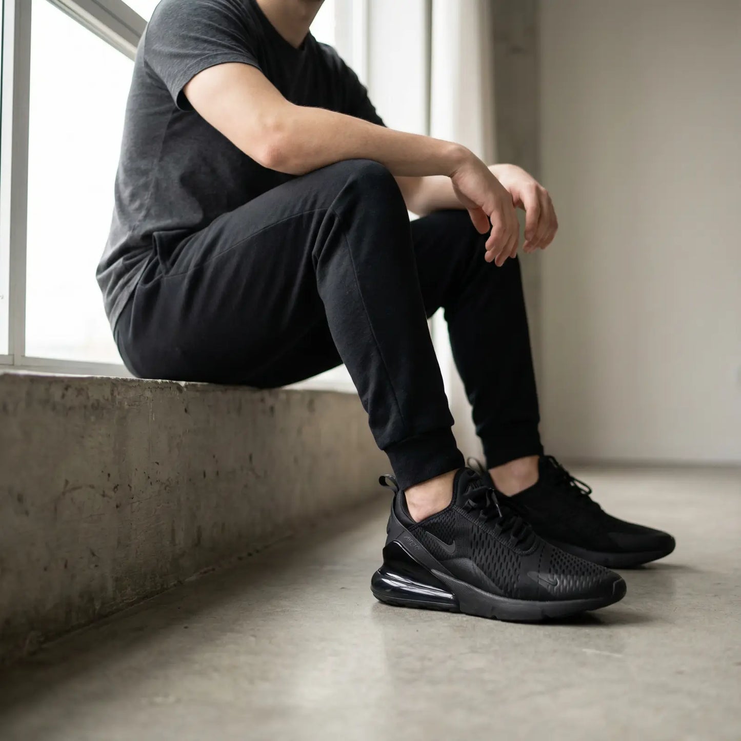 Person wearing black Nike sneakers sitting on a concrete floor.