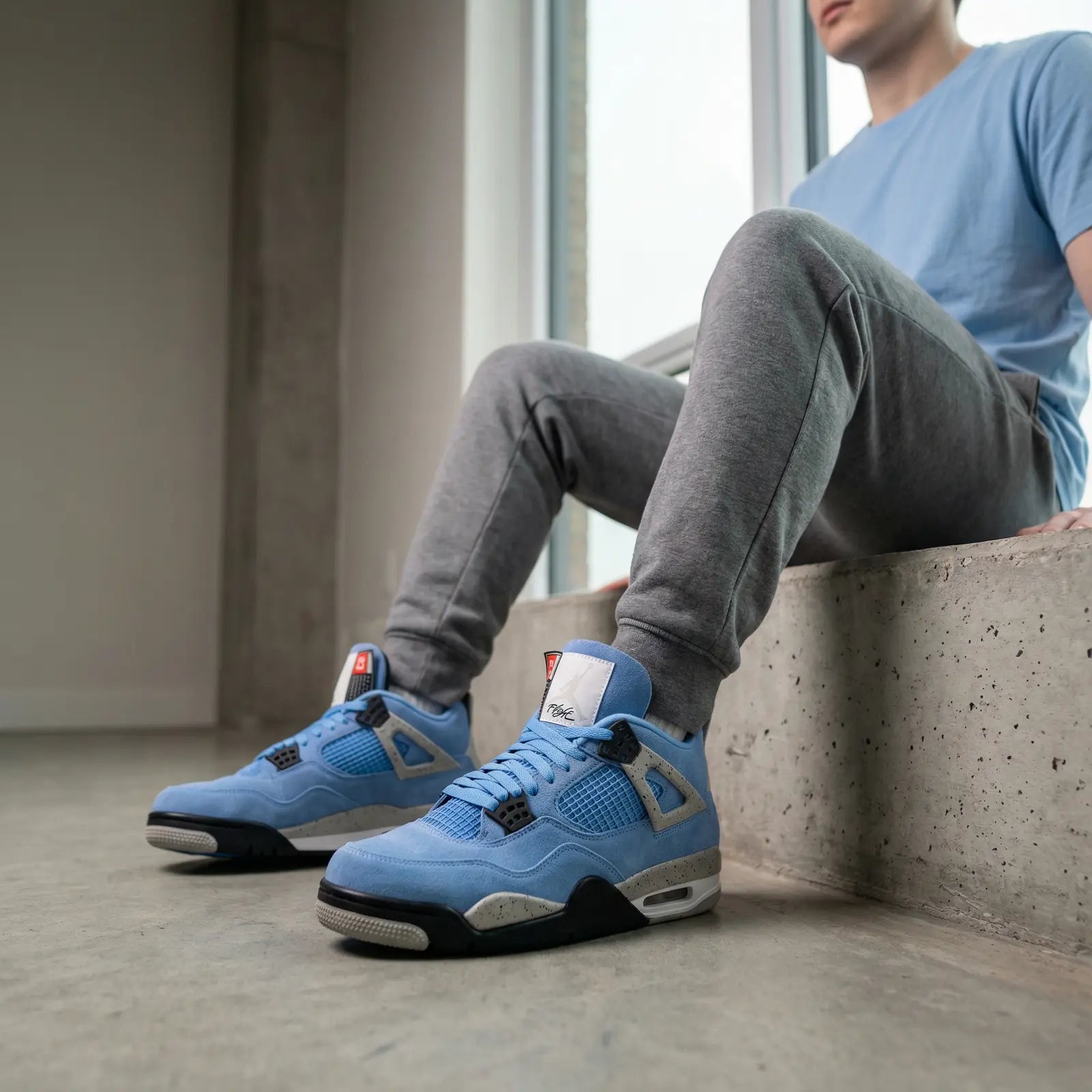Person wearing blue sneakers sitting on a concrete ledge indoors