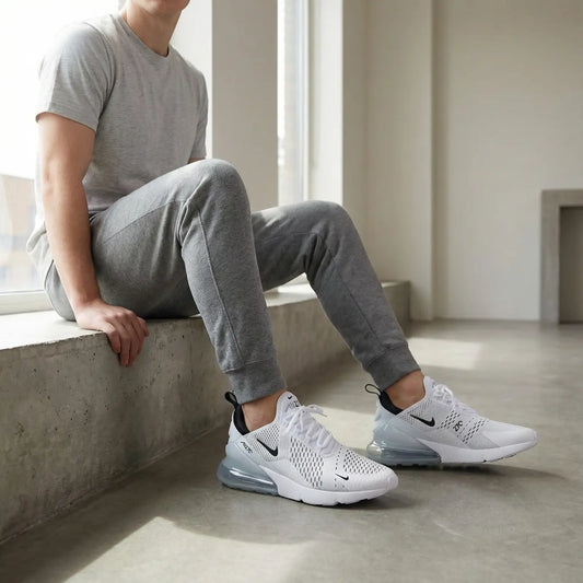 Person wearing gray tracksuit and white Nike sneakers sitting on a concrete ledge.